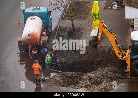 Ukraine, Romny, December 24, 2024: Construction workers repair a damaged underground pipeline using heavy equipment, including a backhoe loader and a Stock Photo