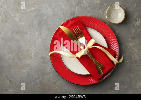 Beautiful plates, sauce bowl, golden cutlery and red napkin on gray textured table, flat lay. Space for text Stock Photo
