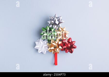 Christmas and New Year, conceptual composition. Creative fir tree made of holiday bow and ribbon on gray-blue background. Top view, copy space. Stock Photo