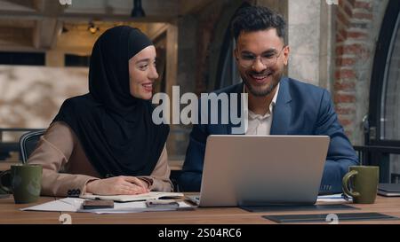 Two business colleagues co-workers talk discuss corporate work at office cafe multiracial male female employees Indian man muslim woman in hijab Stock Photo