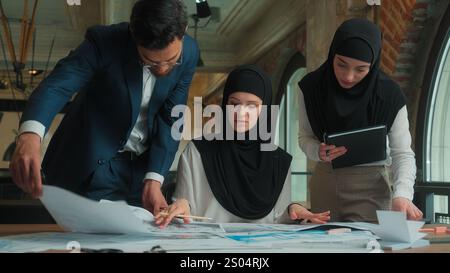 Muslim designer architect in hijab working in office drawing blueprints architecture project on desk business man women multiethnic team colleagues Stock Photo