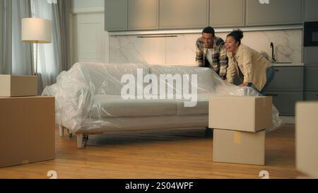 Happy satisfied couple home owners moving in new house relocation African American family move couch buy furniture sofa delivery woman man in love Stock Photo
