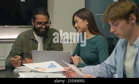 Happy team coworkers colleagues managers man woman talk laugh discuss project on laptop business startup analyzing graphs paperwork diverse Stock Photo