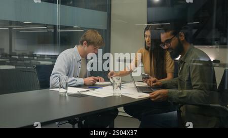 Group of coworkers woman men colleagues managers diverse businesswoman businessmen sit at table office boardroom team work with devices analyzing Stock Photo