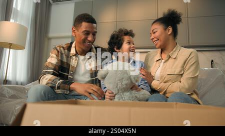 Happy little boy son kid open box unpacking parcel take teddy bear fluffy toy birthday present surprise excited joyful child smiling love parents Stock Photo