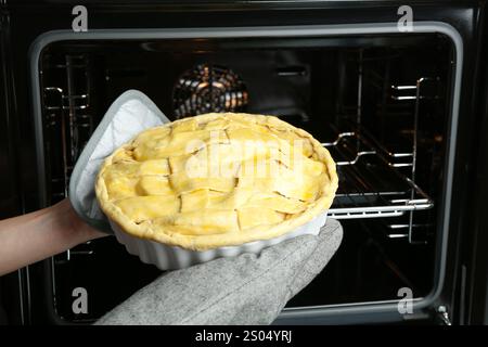 Woman putting homemade apple pie into oven in kitchen, closeup Stock Photo