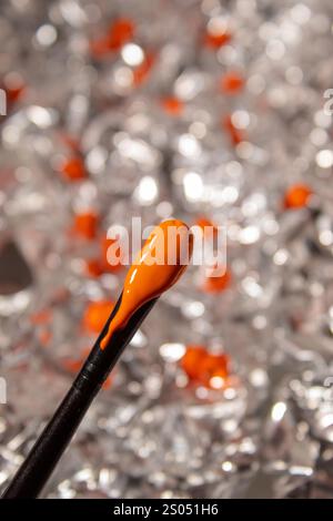 Brush with orange color close up with background of crumpled aluminum foil Stock Photo