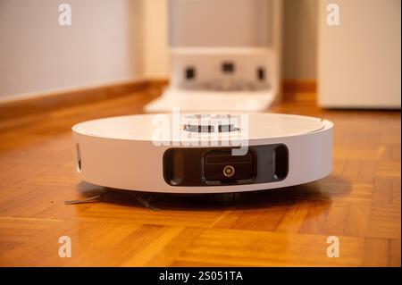 Robot vacuum cleaner with camera and sensors cleans a wooden floor Stock Photo