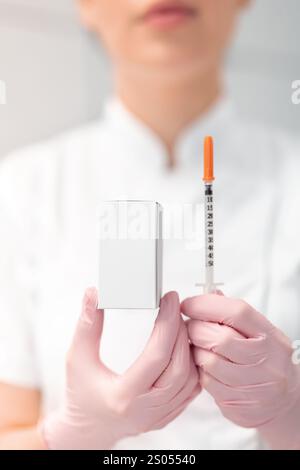 Unrecognizable female dermatologist holding injection syringe and medicine box with blank space in clinic. Anonymous cosmetologist in beauty spa salon.  Stock Photo