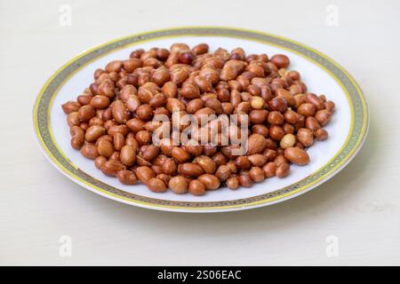 Close-up of roasted peanuts in a white plate on a wooden surface. Stock Photo