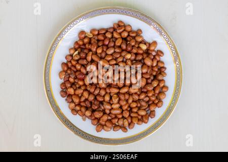 Top view of roasted peanuts in a white plate on a wooden surface. Stock Photo