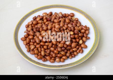 Spicy roasted peanuts in a white plate on a wooden surface. Stock Photo