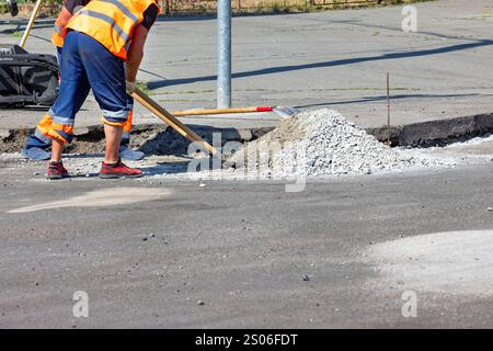 Under the warm sun, a diligent construction worker in vibrant gear performs road repairs, using a shovel to work with gravel. Copy space. Stock Photo