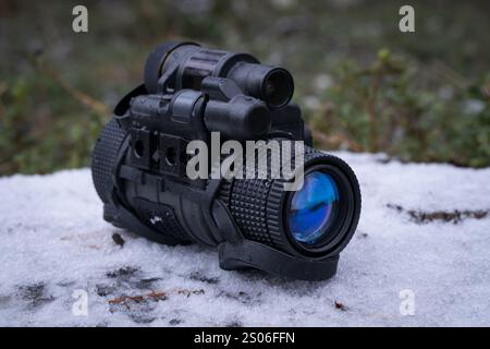 Modern military night vision monocular of the 3rd generation on a stump in a winter forest. Stock Photo