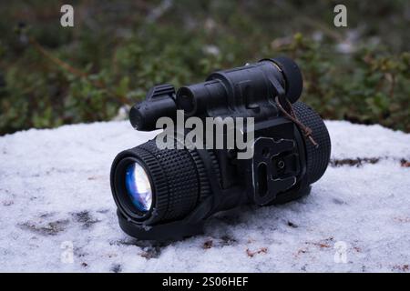 Modern compact military night vision monocular 3rd generation on a stump in a winter forest. Stock Photo