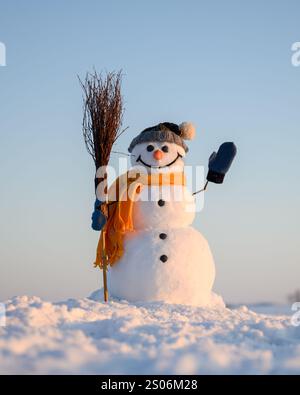 Funny snowman with broom and yellow scarf on snowy field. Blue sky on background Stock Photo