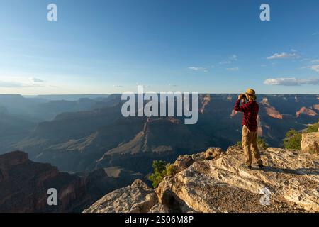 Guy looking at binoculars in hill. man in t-shirt with backpack. Young Caucasian man during hike in valley landscape Stock Photo