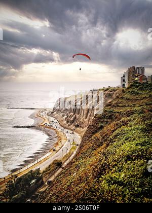 A hang glider soars gracefully along the dramatic coastline of Lima, Peru, riding the ocean breezes high above the cliffs. Stock Photo