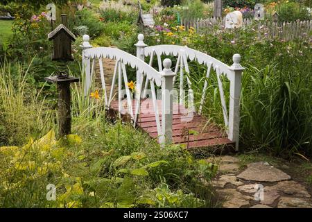 Flagstone path and white and brown wooden footbridge next to birdhouse in backyard rustic garden in summer. Stock Photo