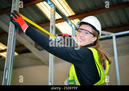 Construction worker using measuring tape while mounting plasterboard in a new building Stock Photo