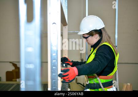 Female construction worker using spirit level while mounting plasterboard on metal frame Stock Photo