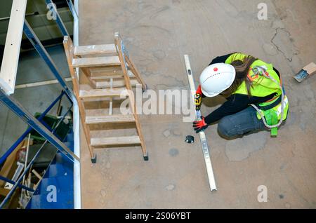 Female construction worker installing metal frame using spirit level and cordless drill, preparing for plasterboard or fiber mounting Stock Photo