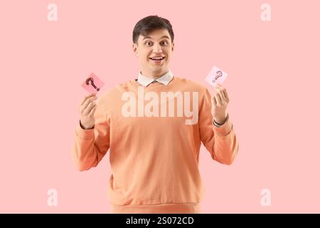 Young man holding sticky notes with question marks on pink background Stock Photo