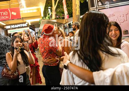 Melbourne, Australia. 25th Dec, 2024. Pedestrians take photos with their mobile phones while a couple kiss on a street during Christmas Celebrations in Melbourne. Crowds celebrate Christmas night at Melbourne's Flinders Street Station, adorned with festive lights and decorations, enjoying the lively atmosphere and summer cheer. Credit: SOPA Images Limited/Alamy Live News Stock Photo