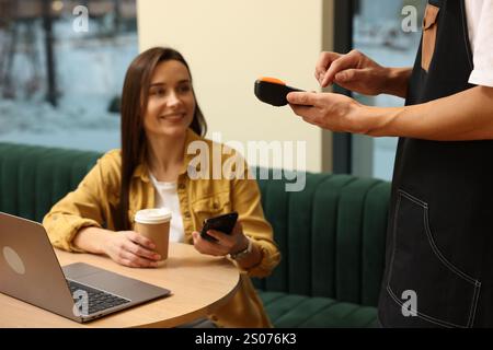 Waiter taking payment from client via terminal in cafe, selective focus Stock Photo