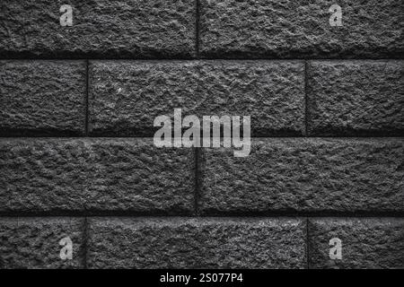 A textured wall of dark gray bricks, with a rough and uneven surface. The bricks are arranged in a traditional pattern, creating a sense of order and Stock Photo