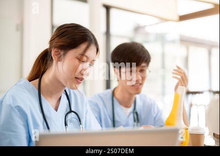 A beautiful, smart Asian female medical student in scrubs is examining a model of bone joints and discussing it with her classmate while studying toge Stock Photo