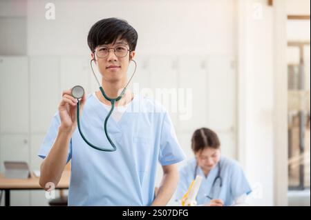 A smart Asian male medical student in scrubs is examining a model of ...