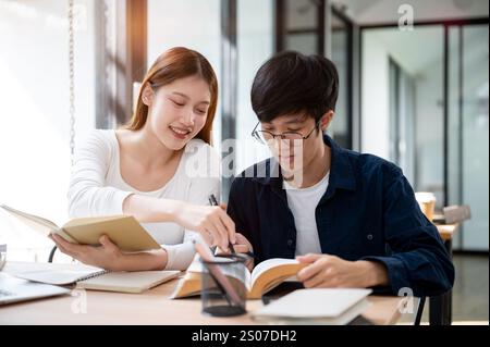 Two young Asian college students are studying and preparing for an exam together in a coffee shop or the campus library reading area, discussing a top Stock Photo