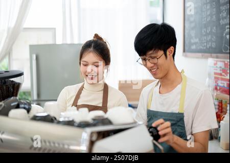 Two friendly and happy young Asian coffee shop staff members or baristas are preparing coffees to serve to customers while working in the coffee shop. Stock Photo