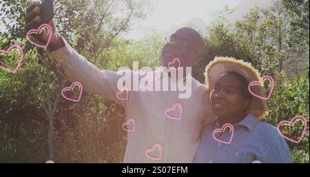 Image of hearts over senior african american couple taking selfie at christmas Stock Photo