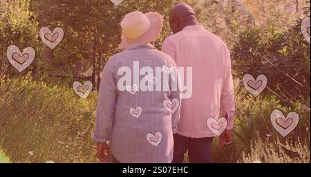 Image of hearts over senior african american couple walking in garden at christmas Stock Photo