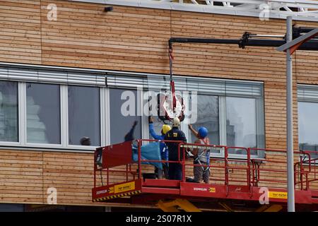 Workers on a building site installing new windows at height at the Village Im Dritten housing development, Vienna, Austria, June 2024 Stock Photo