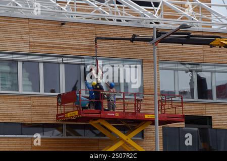 Workers on a building site installing new windows at height at the Village Im Dritten housing development, Vienna, Austria, June 2024 Stock Photo