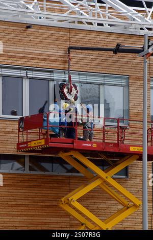 Workers on a building site installing new windows at height at the Village Im Dritten housing development, Vienna, Austria, June 2024 Stock Photo