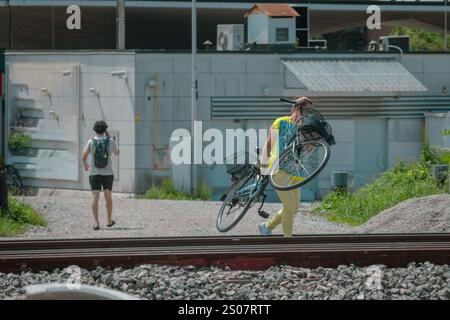 Woman carrying bicycle illegaly over railroad or train tracks in Ljubljana. Dangerous and forbidden jumping the tracks with live train traffic... Stock Photo