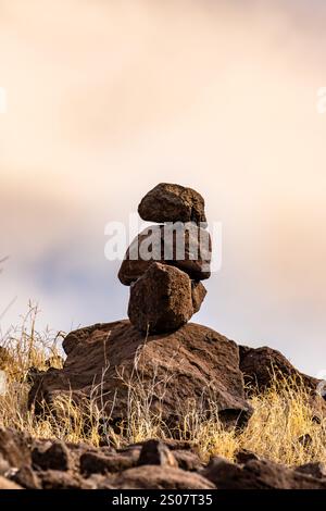 Stacked stone cairn pyramid standing on grassy hill slope beside green ...