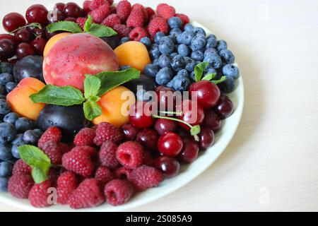 Delicious mix of colorful summer fruits lying on white plate, decorated with fresh mint leaves Stock Photo