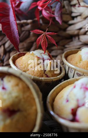 Freshly baked cranberry muffins cooling on a wicker tray, adorned with vibrant autumn leaves, creating a cozy and inviting scene Stock Photo