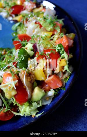 Vibrant salmon salad with fresh ingredients, including avocado, cherry tomatoes, and a sprinkle of mustard seeds, served on a blue plate Stock Photo