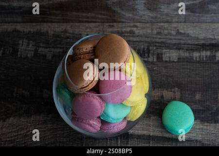 A glass bowl filled with a variety of colored macarons. The macarons are in different colors and are arranged in the bowl Stock Photo