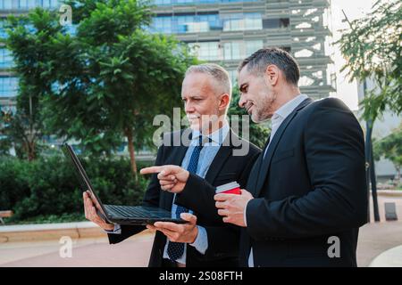 Two professional businessmen discussing work while looking at a laptop, collaborating and brainstorming ideas for a project during a business meeting, wearing suits and maintaining a focused demeanor. High quality photo Stock Photo