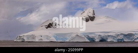 panoramic landscape of sunlight on the snow of the two rocky mountain tops of jacques peaks at the entrance to bancroft bay on the antarctic peninsula Stock Photo