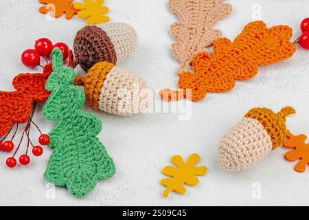 Set of traditional knitted autumn decoration. Crocheted different acorn and leaves, handmade, cozy hobby concept. Fall props on light stone background Stock Photo