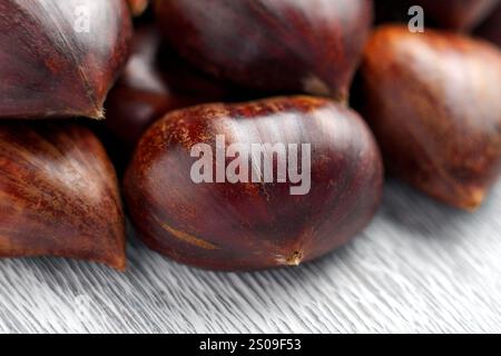 Group of fresh whole chestnuts with glossy nut shells arranged on a gray textured surface. Close up Stock Photo