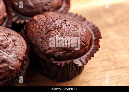 Freshly baked chocolate muffins in brown paper wrappers on a wooden surface. Concept of homemade treats and sweet indulgence Stock Photo